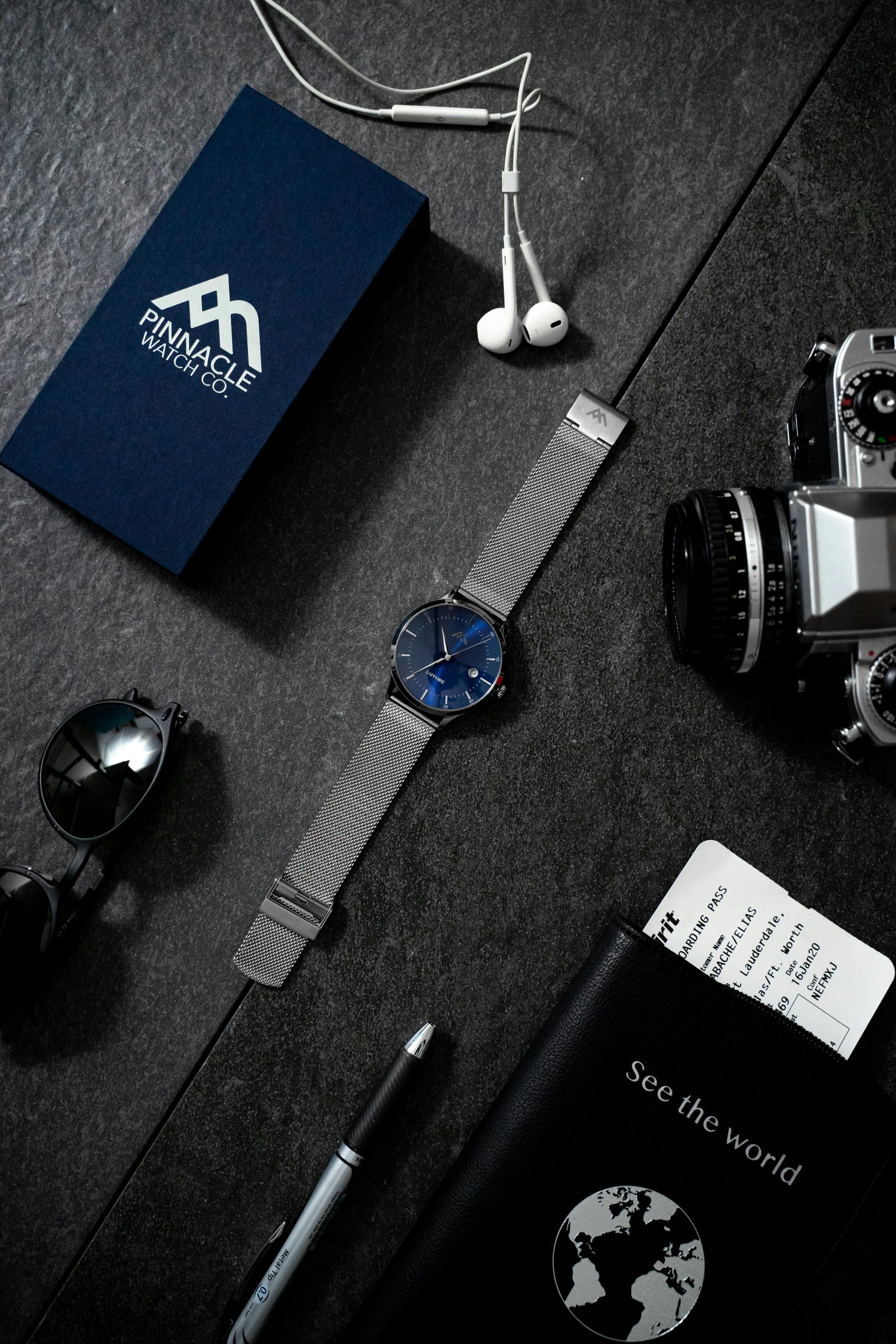 Home Stylish flat lay of watch, camera, passport, and travel items on dark surface.